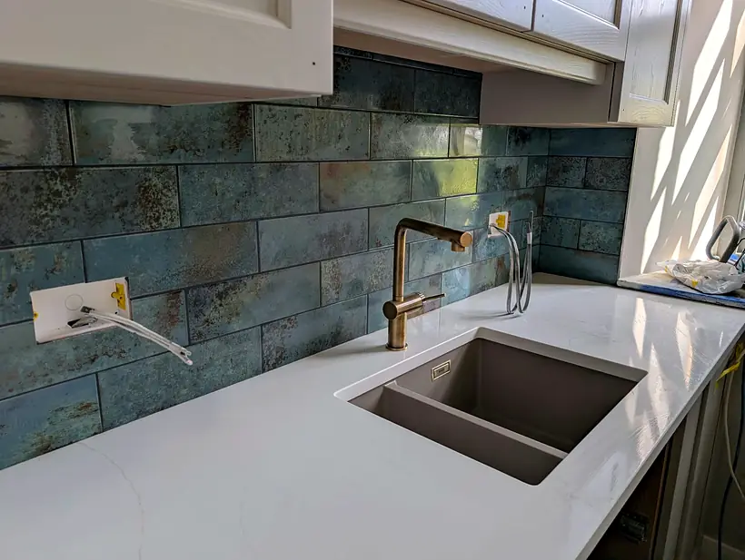 Blue green metallic brick splashback with brass tap